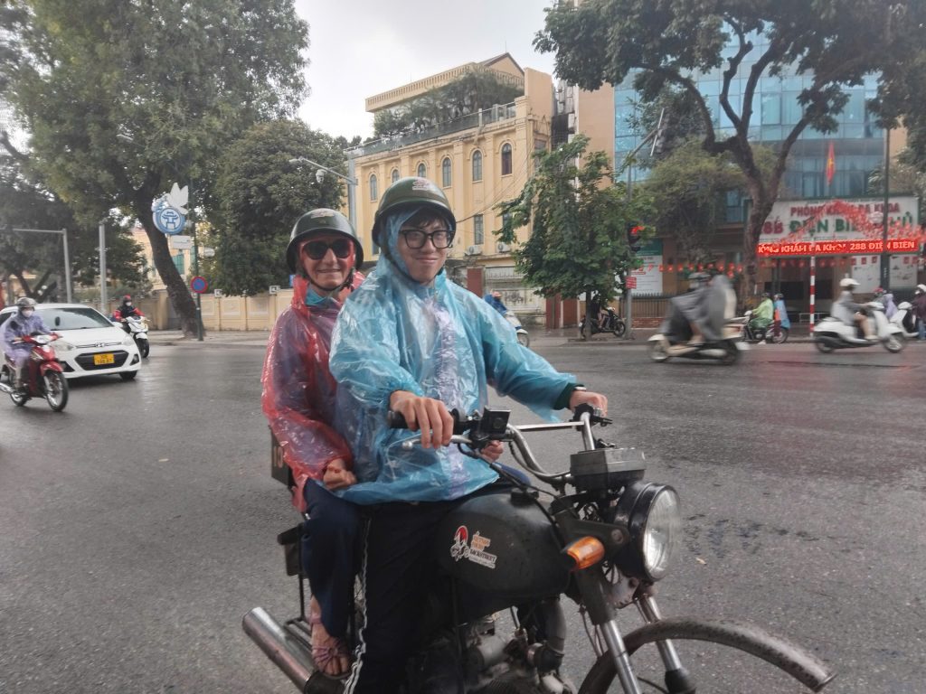 Guests riding vintage Minsk motorcycles during a rainy Hanoi Night Motorbike Tour.