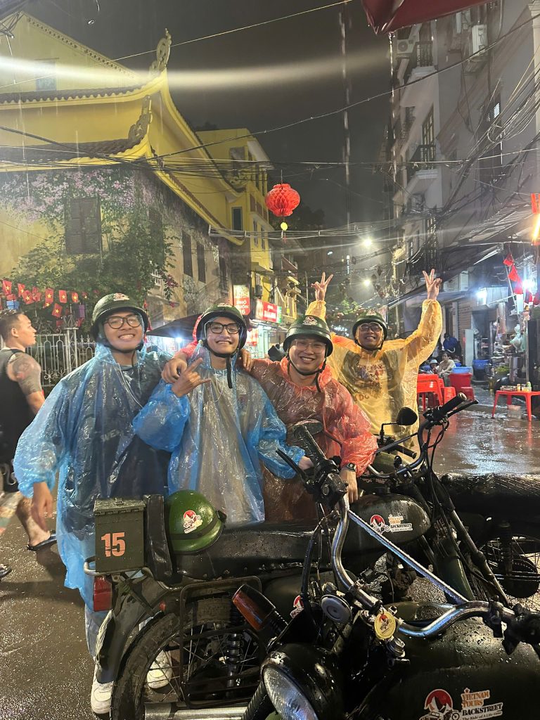 Guests riding vintage Minsk motorcycles during a rainy Hanoi Night Motorbike Tour.