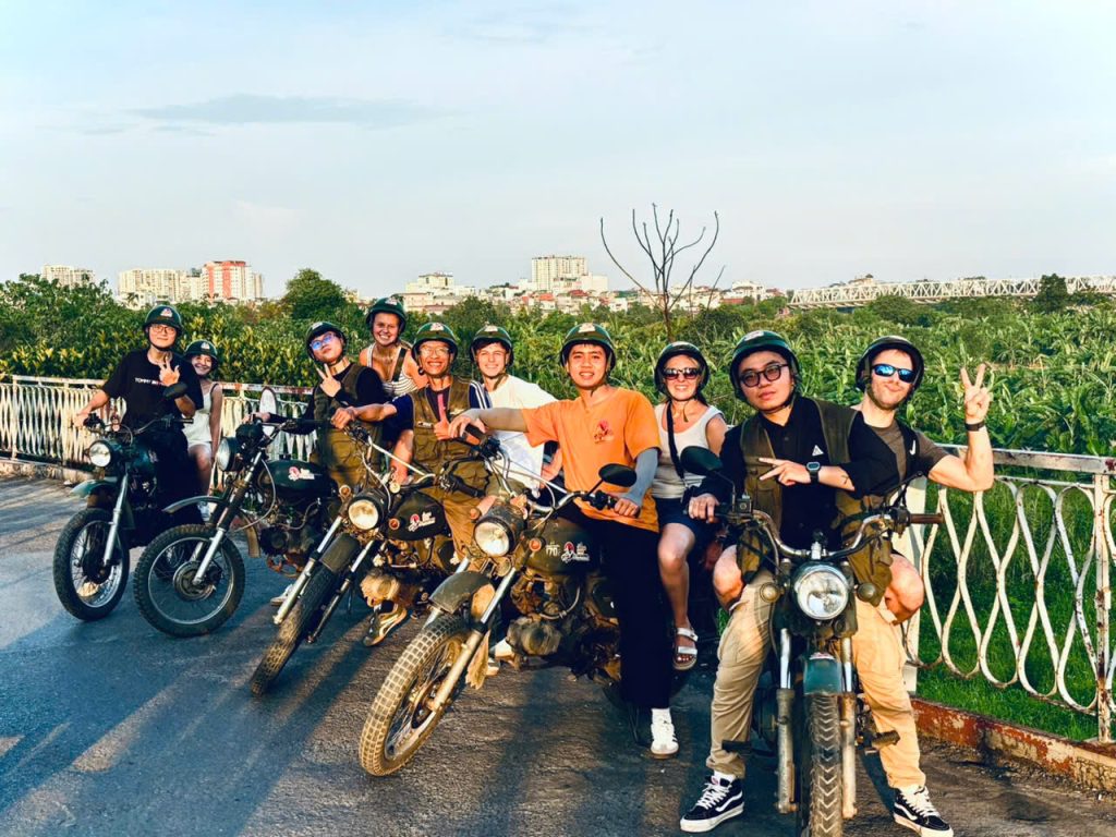 "Guests enjoying a Hanoi Motorbike Tour on Long Bien Bridge at sunset"